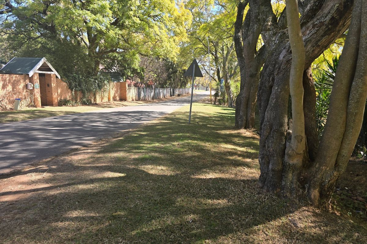 A view of the street frontage featuring mature trees, a grass verge, and a brick boundary wall along the residential property.