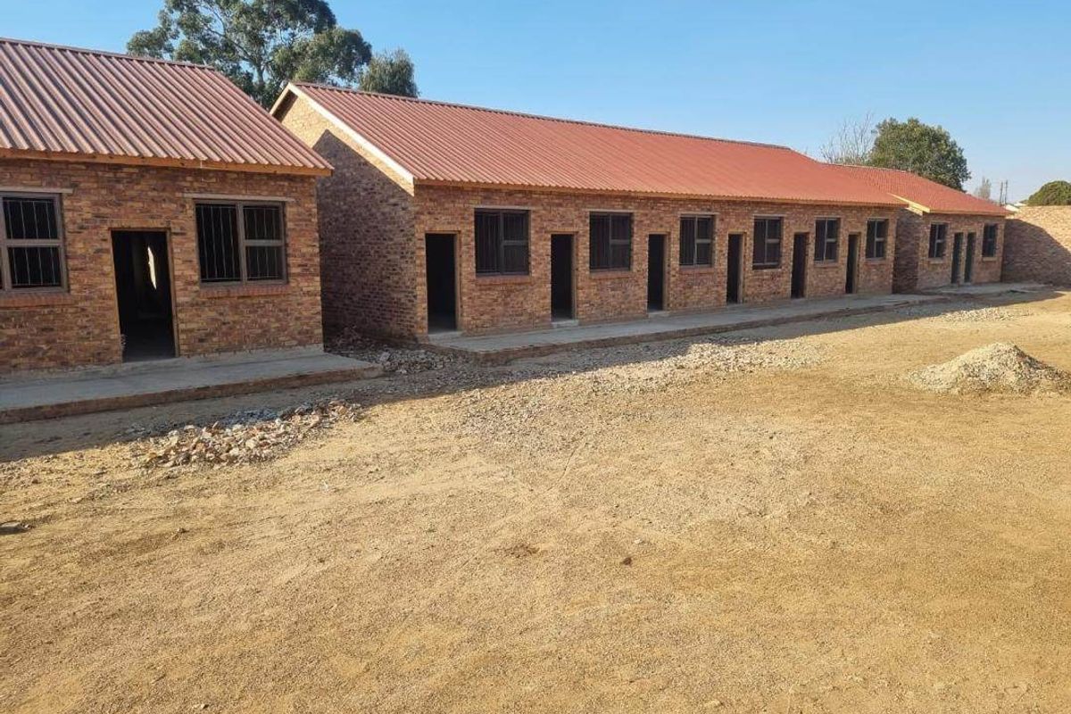 Exterior view of a row of face brick apartment units featuring corrugated metal roofing and steel window frames with security bars.