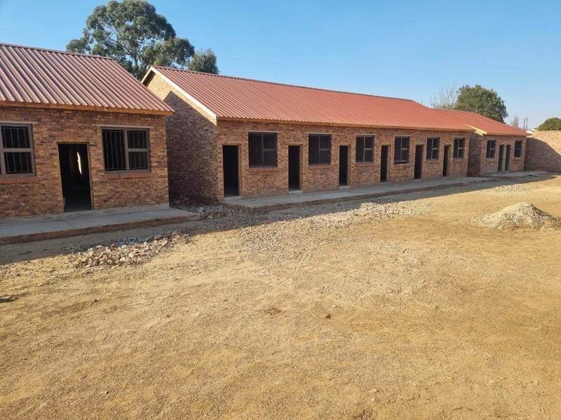 Exterior view of a row of face brick apartment units featuring corrugated metal roofing and steel window frames with security bars.