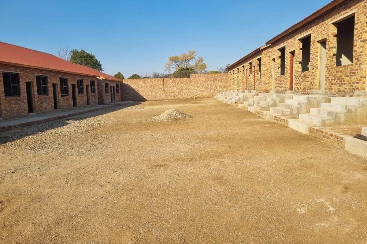 An exterior view of an unfinished apartment complex development featuring exposed brick structures, concrete staircases, and an unpaved courtyard area.