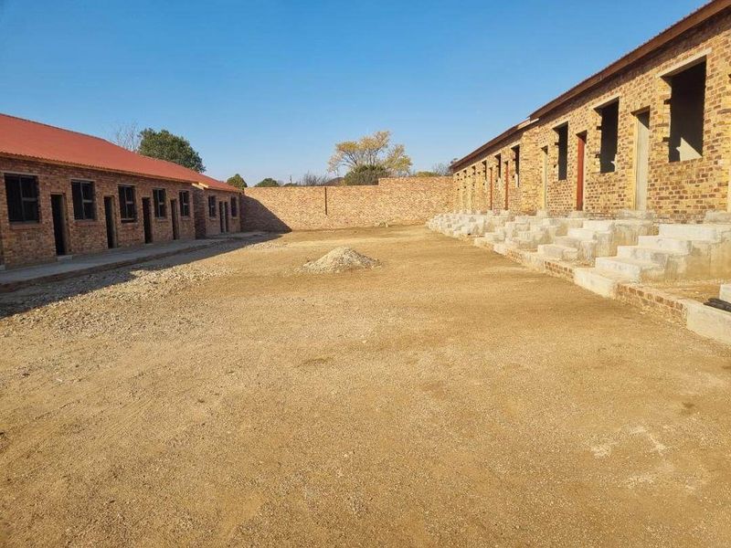 An exterior view of an unfinished apartment complex development featuring exposed brick structures, concrete staircases, and an unpaved courtyard area.