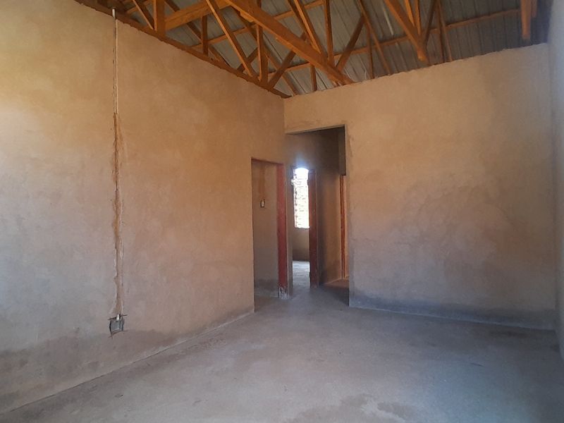 An unfinished interior space featuring exposed timber roof trusses, raw masonry walls, and concrete flooring, currently in a shell construction state.