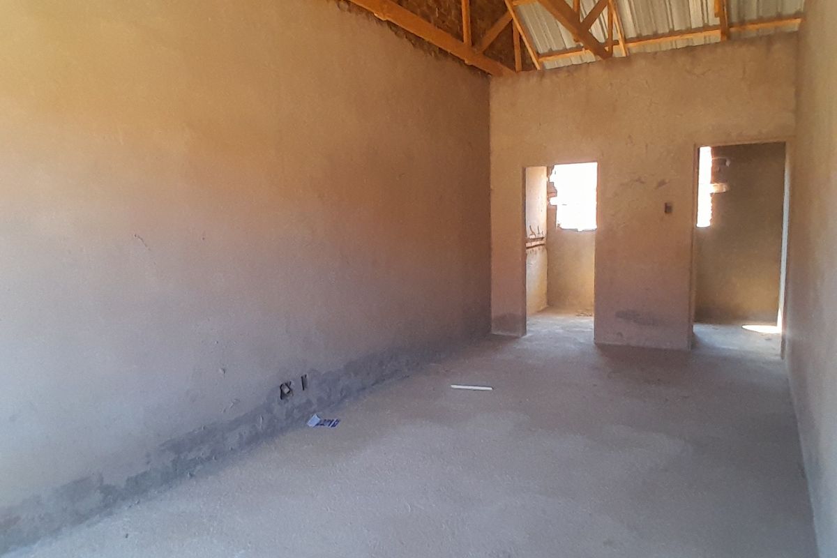 An unfinished interior space featuring exposed timber roof trusses, raw plastered walls, and cement screed flooring, currently in a shell construction state.