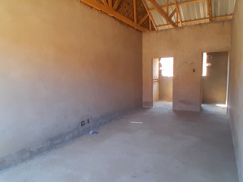 An unfinished interior space featuring exposed timber roof trusses, raw plastered walls, and cement screed flooring, currently in a shell construction state.