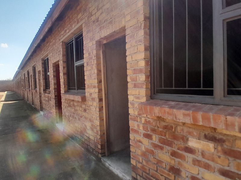 Exterior view of an apartment block featuring exposed brick walls, metal-framed windows with security bars, and a concrete walkway.
