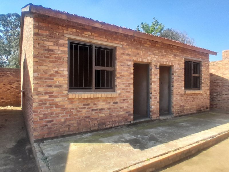 Exterior view of a single-story brick building featuring a concrete patio, security-barred windows, and a tiled roof.