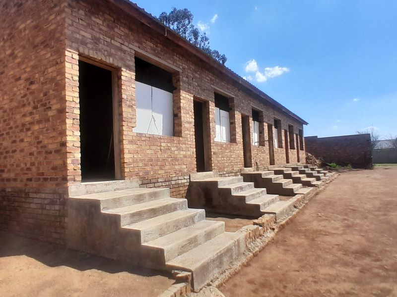 An exterior view of an unfinished brick building featuring multiple entrances with concrete steps, currently in a shell construction state.