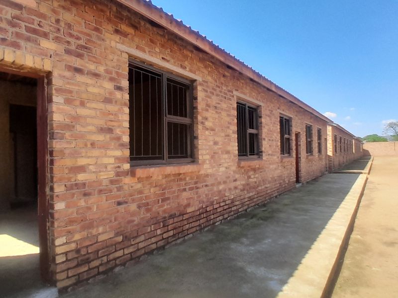 Exterior view of a long brick building featuring multiple windows with security bars and a concrete walkway along the side.