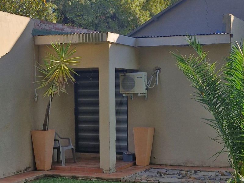 A small covered patio area featuring an external air conditioning unit and tiled flooring, requiring some maintenance to the exterior wall.
