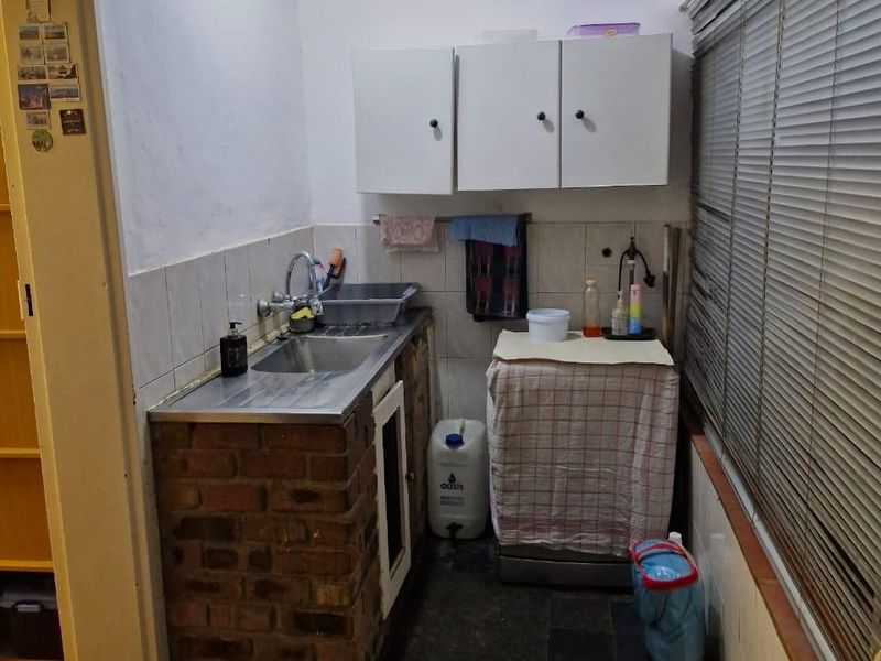 A functional laundry area featuring a stainless steel sink, brick-based cabinetry, wall-mounted storage cupboards, and slate flooring.