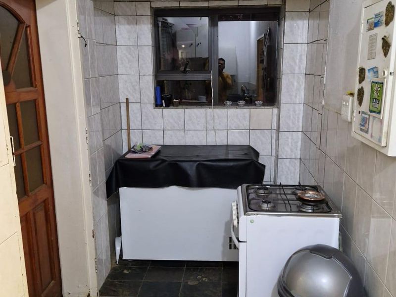 A functional scullery or utility area featuring tiled walls, a gas stove, and direct access to the exterior via a timber door.