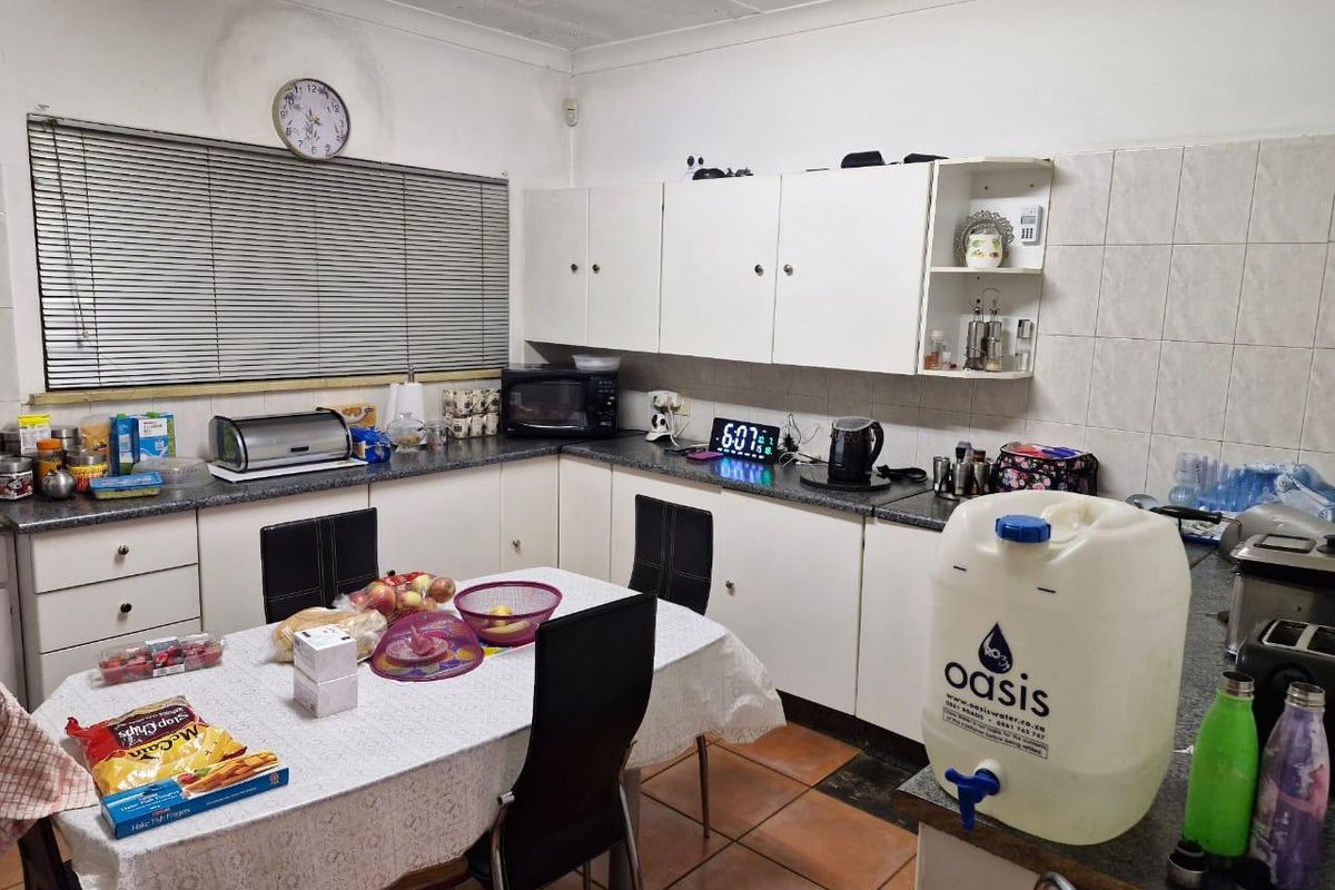A functional kitchen featuring white built-in cabinetry, laminate countertops, and tiled flooring, currently showing signs of wear and ceiling water damage.