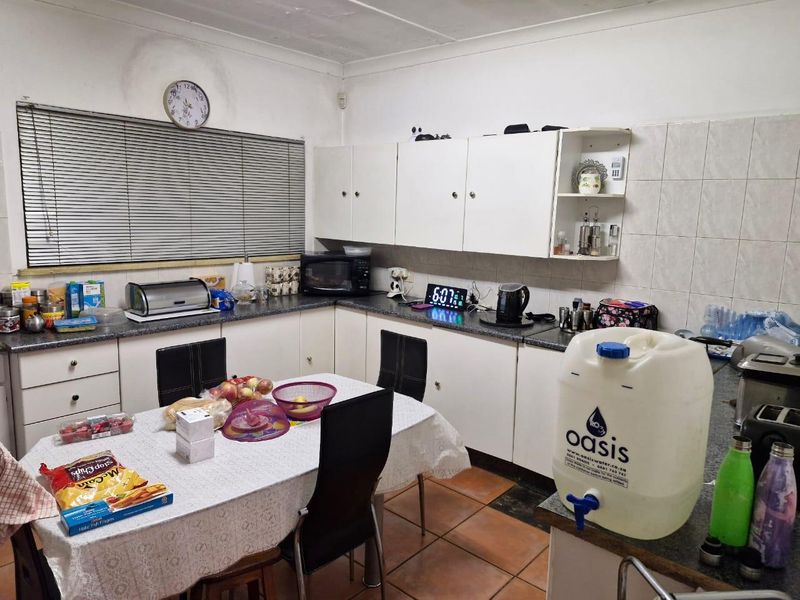 A functional kitchen featuring white built-in cabinetry, laminate countertops, and tiled flooring, currently showing signs of wear and ceiling water damage.