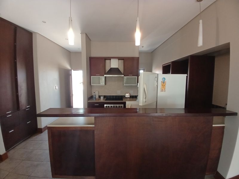 A functional kitchen featuring dark wood cabinetry, a breakfast bar, tiled backsplash, and built-in extractor fan, offering a practical layout for daily use.