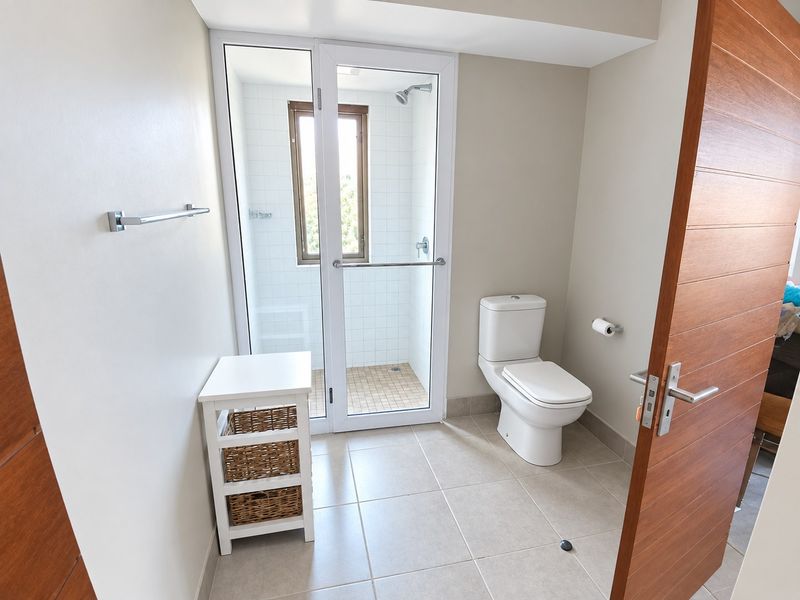 A clean, modern bathroom featuring a separate shower enclosure with white tiling, a standard toilet, and neutral floor tiles.