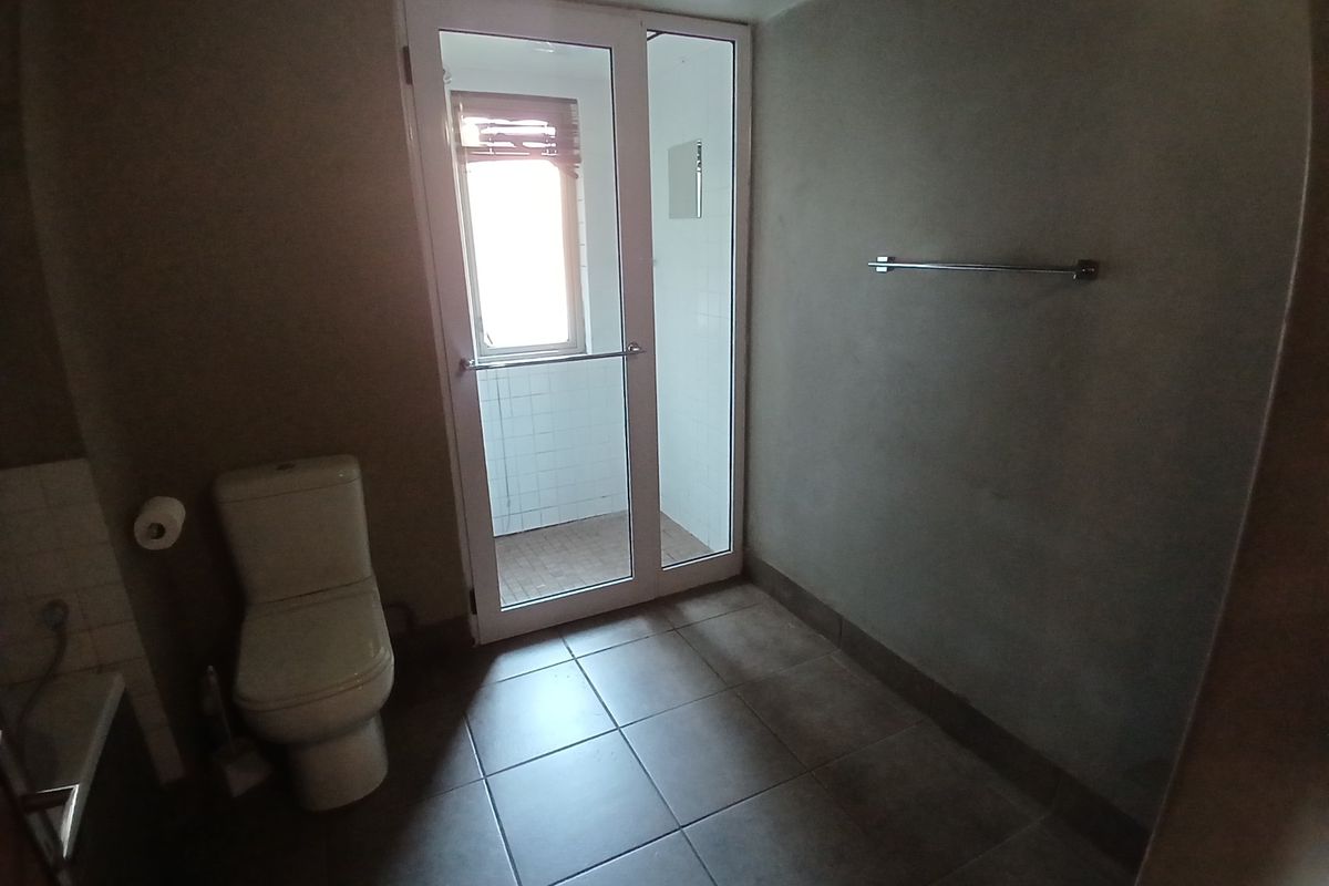 A functional bathroom featuring tiled flooring, a toilet, and a separate shower enclosure accessed via a glass door.
