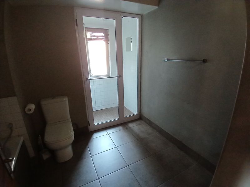 A functional bathroom featuring tiled flooring, a toilet, and a separate shower enclosure accessed via a glass door.