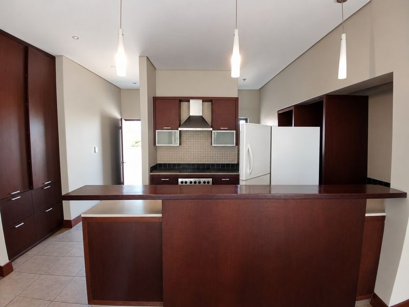 A clean, modern kitchen featuring dark wood cabinetry, a breakfast bar, tiled backsplash, and integrated stainless steel extractor fan.