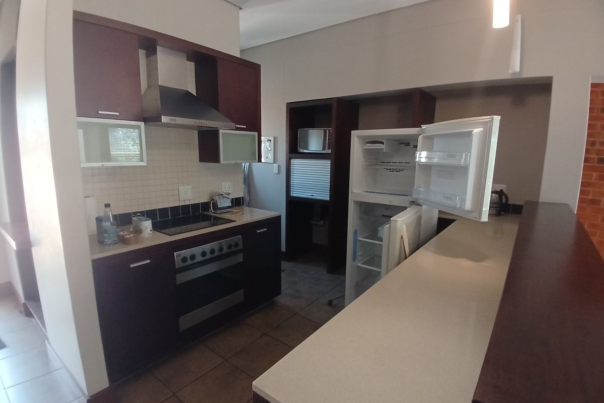 A functional kitchen featuring dark wood cabinetry, stone countertops, a breakfast bar, and integrated appliances including an oven and extractor fan.