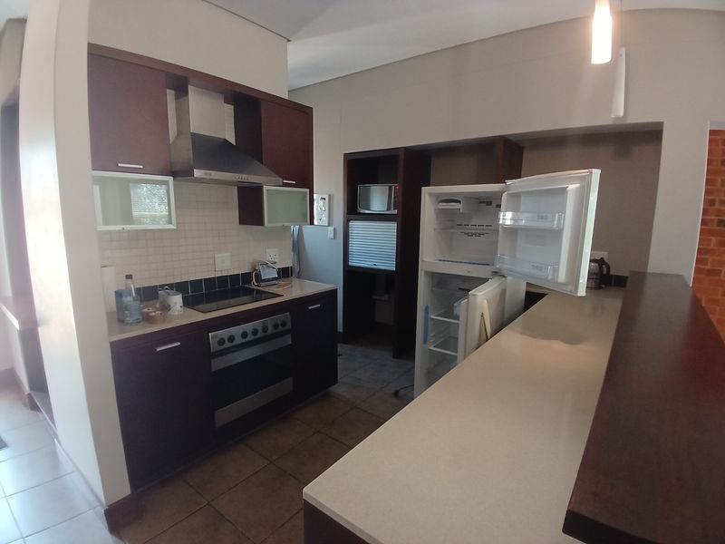 A functional kitchen featuring dark wood cabinetry, stone countertops, a breakfast bar, and integrated appliances including an oven and extractor fan.
