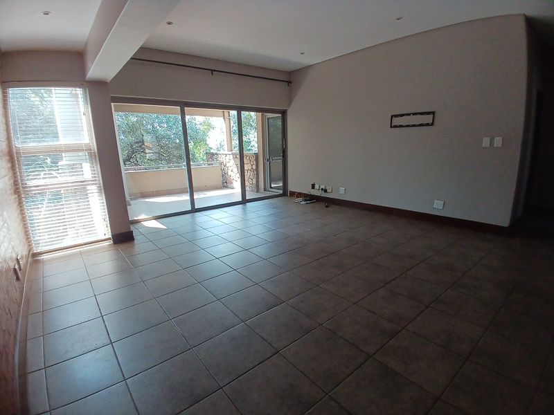 A spacious, empty living area featuring tiled flooring, recessed lighting, and large sliding glass doors that provide access to an outdoor balcony.
