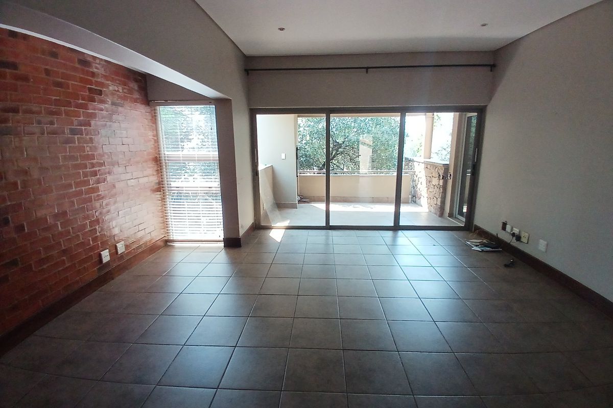 Spacious living area featuring an exposed brick accent wall, tiled flooring, and large sliding glass doors leading to an outdoor balcony.