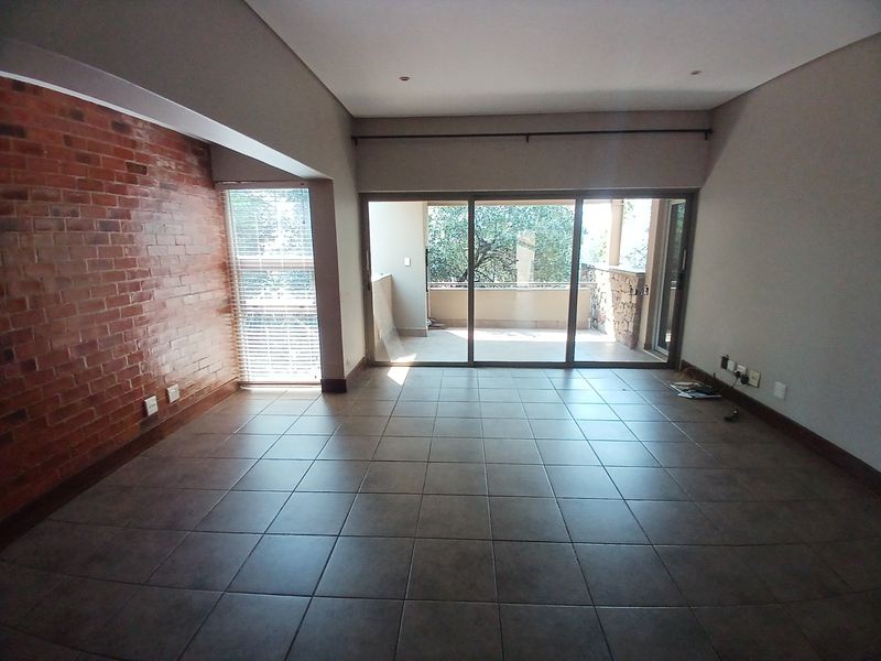 Spacious living area featuring an exposed brick accent wall, tiled flooring, and large sliding glass doors leading to an outdoor balcony.