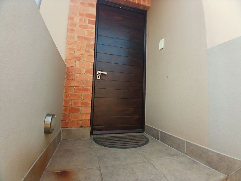A private apartment entrance featuring a dark wood door, brick accent wall, and tiled flooring with an exterior wall light.