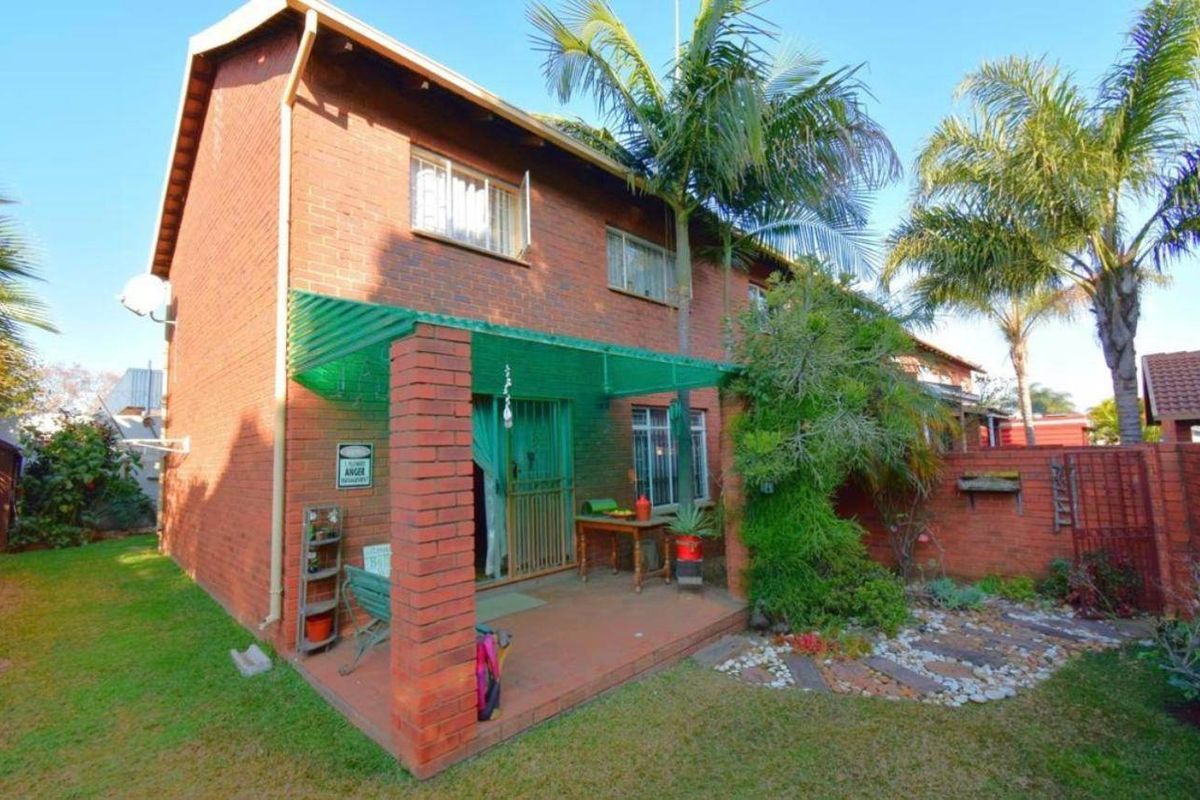 Rear view of a double-story brick townhouse featuring a covered patio area, brick boundary walls, and a small garden space.