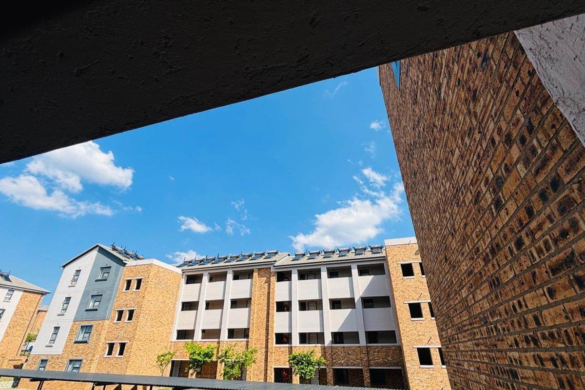View of the apartment complex exterior featuring brick facade construction and roof-mounted solar water heating panels.