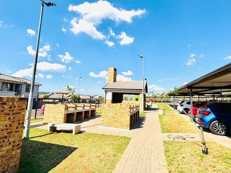 Communal outdoor area featuring a brick braai facility, paved walkways, and covered parking bays within the apartment complex.