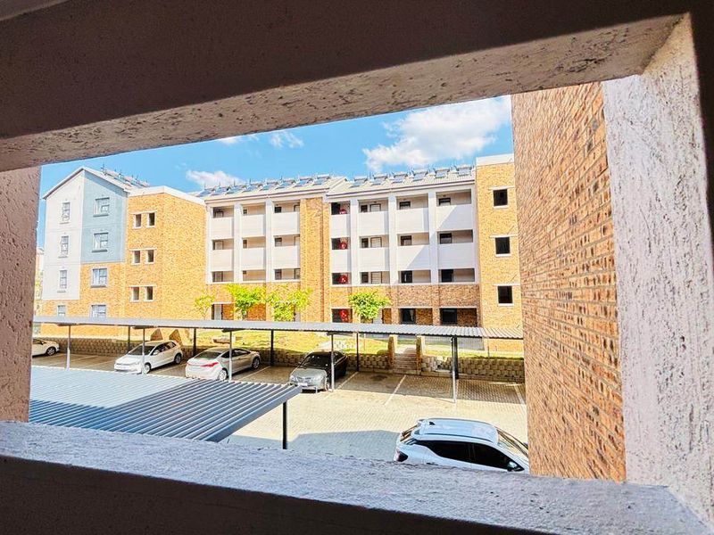 A view from an apartment window overlooking the complex parking area, carports, and adjacent residential building blocks.