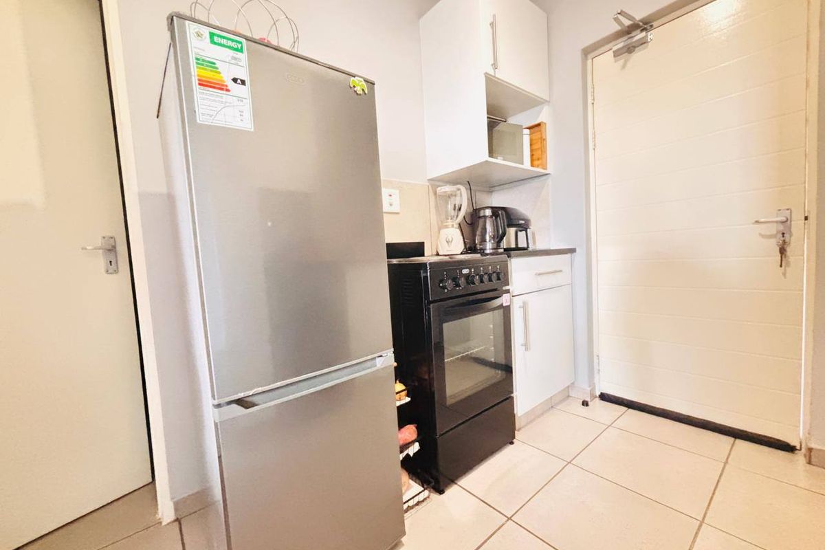 A compact kitchen area featuring built-in cabinetry, a freestanding oven and hob, and tiled flooring, providing a functional space for meal preparation.