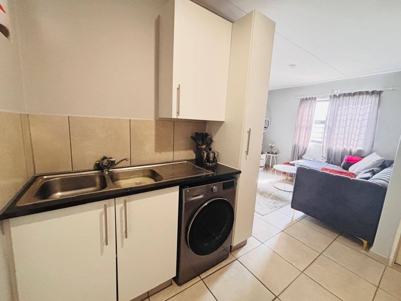 Open-plan kitchen and living area featuring tiled flooring, built-in cabinetry, and a double sink, seamlessly flowing into the adjacent lounge space.