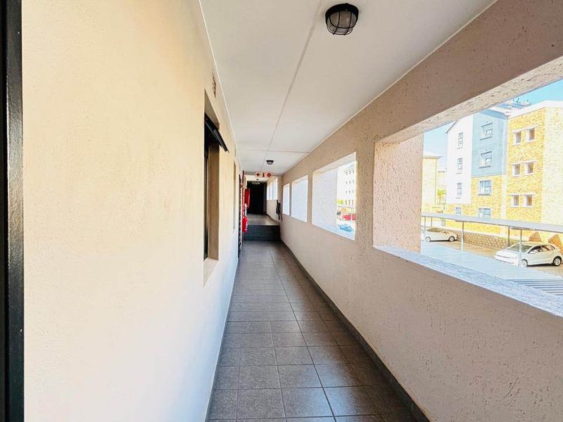 A bright, open-air apartment hallway featuring tiled flooring and a functional ceiling light, providing access to residential units.