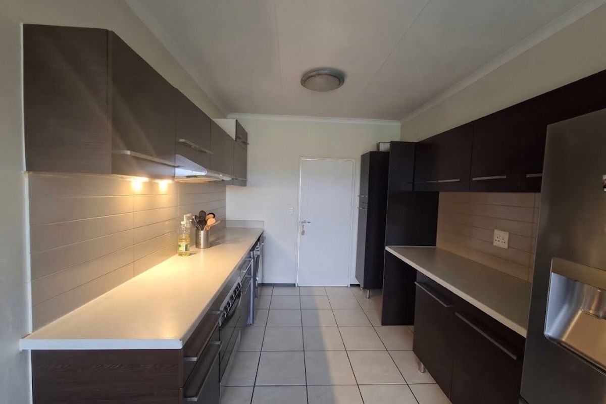 A functional galley-style kitchen featuring dark wood-finish cabinetry, light-colored countertops, tiled backsplash, and ceramic floor tiles with integrated lighting.