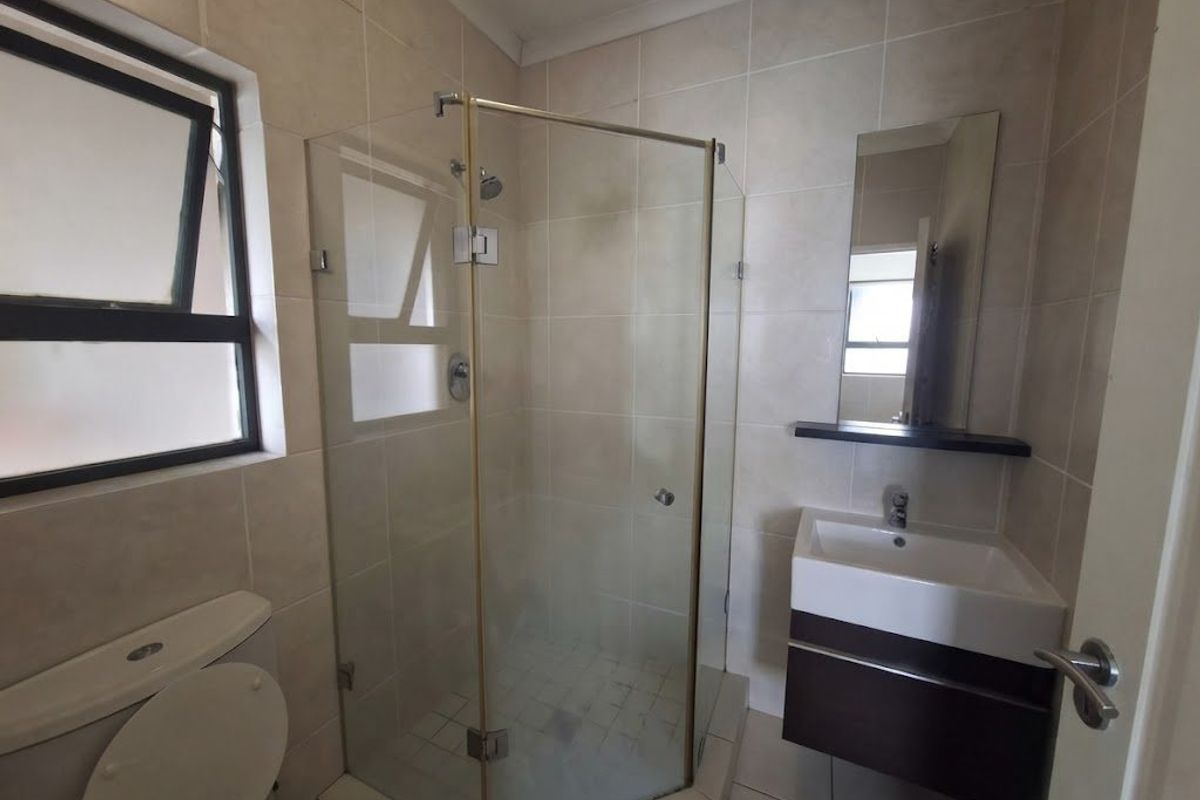 A functional bathroom featuring a glass shower enclosure, wall-mounted vanity with basin, and neutral wall tiling.