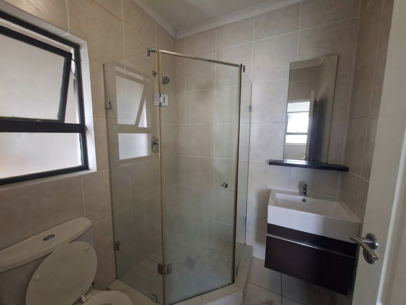 A functional bathroom featuring a glass shower enclosure, wall-mounted vanity with basin, and neutral wall tiling.