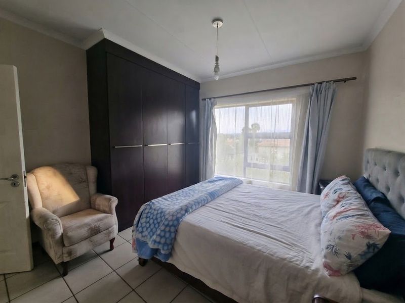 A bedroom featuring built-in dark wood cupboards, tiled flooring, and a window with natural light.