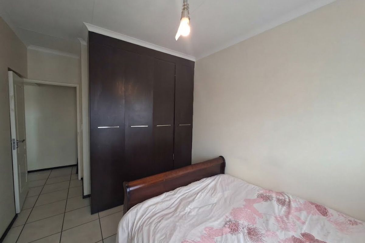 A bedroom featuring dark wood built-in cupboards, tiled flooring, and a coved ceiling, providing a functional and neutral living space.