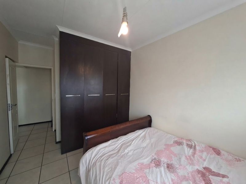 A bedroom featuring dark wood built-in cupboards, tiled flooring, and a coved ceiling, providing a functional and neutral living space.