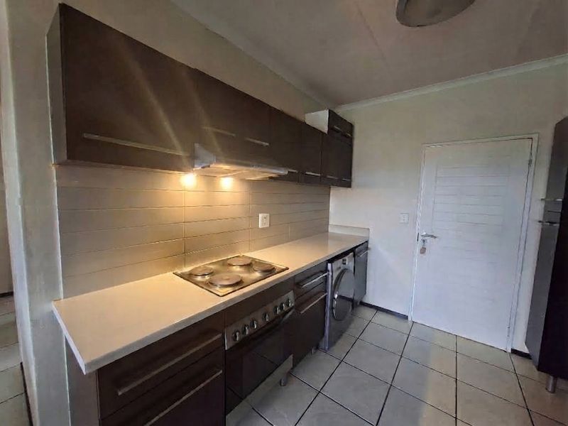 A functional kitchen featuring dark wood cabinetry, a tiled backsplash, built-in electric hob and oven, and integrated laundry appliance space.