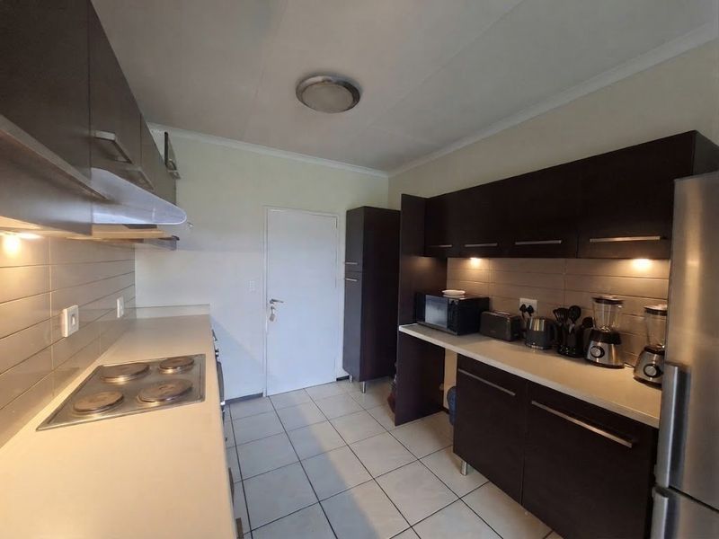 A functional kitchen featuring dark wood cabinetry, a tiled backsplash, an electric hob with extractor fan, and tiled flooring.