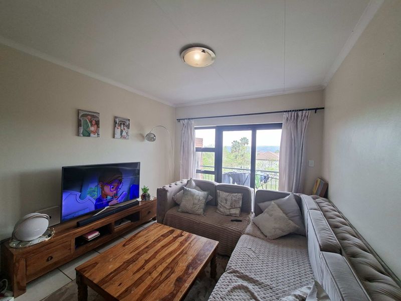 A comfortable living room featuring tiled flooring, a ceiling light fixture, and a sliding glass door providing access to an outdoor balcony area.