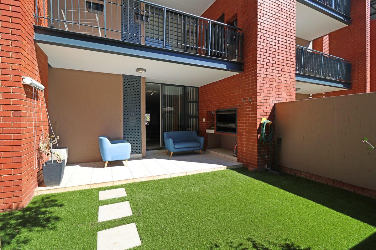 A private rear courtyard featuring a tiled patio, built-in braai, and artificial lawn, with direct access to the interior via sliding glass doors.