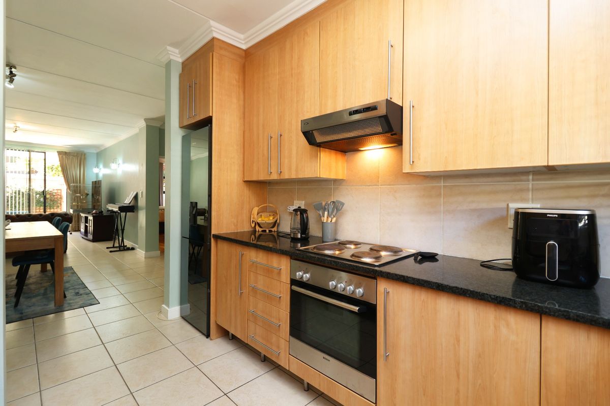 A functional kitchen featuring light wood cabinetry, granite countertops, integrated oven and hob, and tiled flooring, flowing into an open-plan living area.