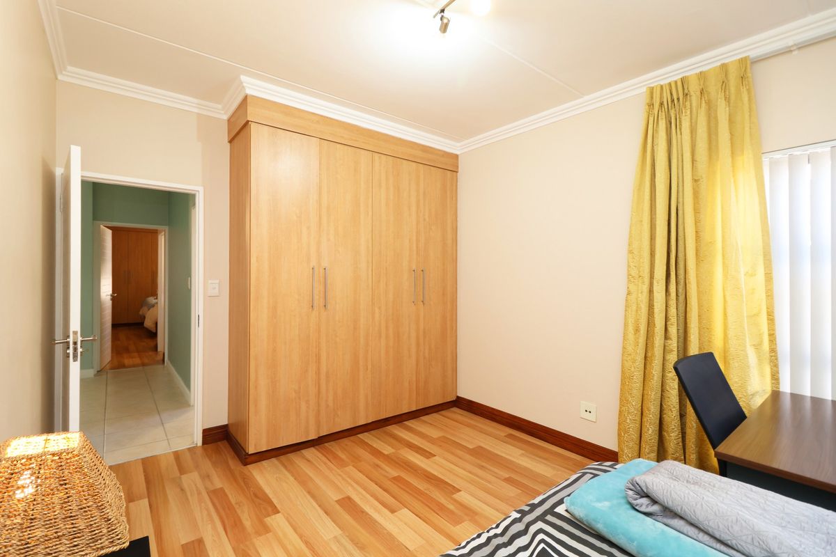 A well-maintained bedroom featuring light wood-look laminate flooring, built-in cupboards, and decorative coving.