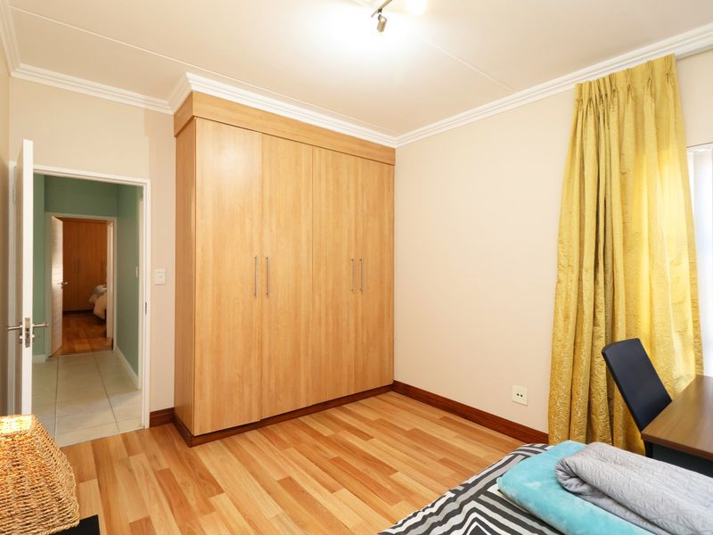 A well-maintained bedroom featuring light wood-look laminate flooring, built-in cupboards, and decorative coving.