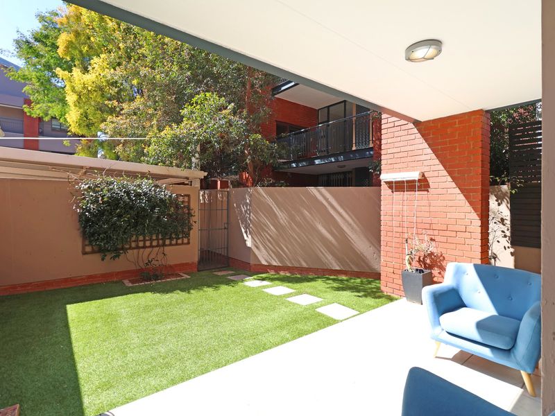 A covered patio area featuring a brick pillar, concrete flooring, and a private rear garden with artificial turf and boundary walling.