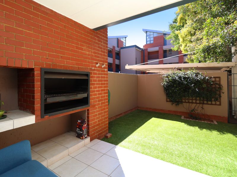 Covered patio area featuring a built-in brick braai, tiled flooring, and a private garden space with artificial lawn.